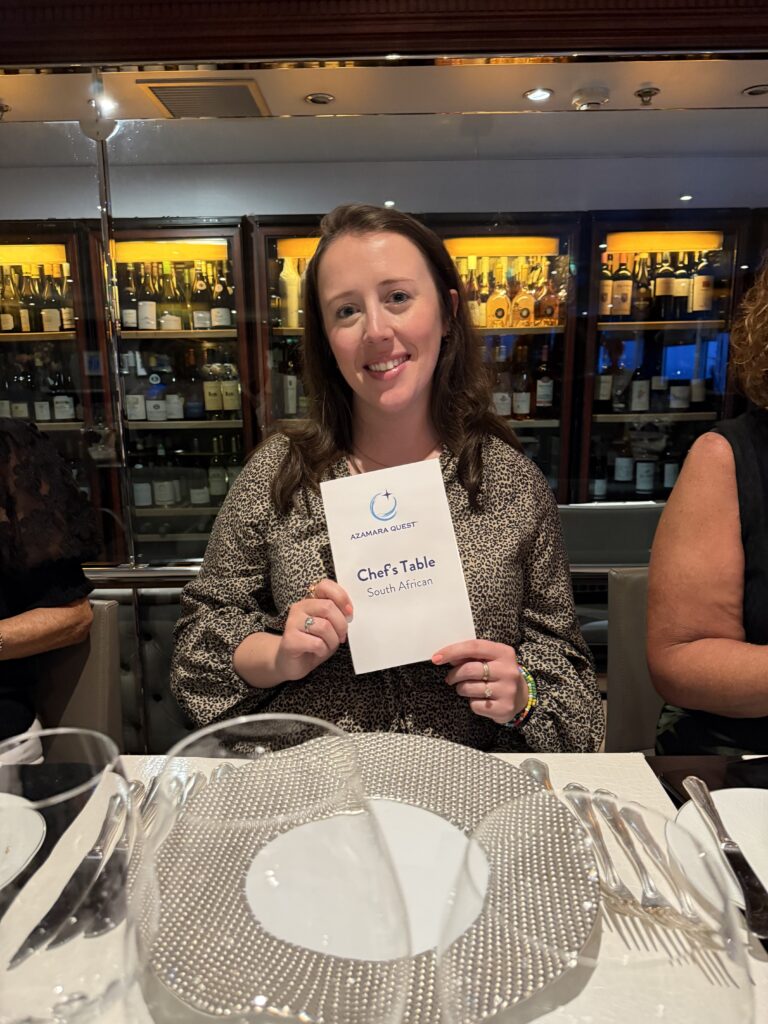 Image of Kathryn at the Chef's Table on the Azamara South Africa cruise with the wine storage in the background. 