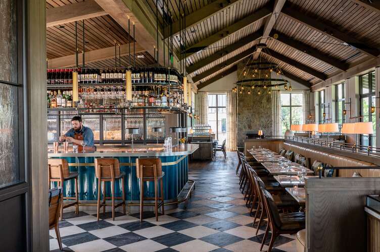 Marigold by Jean-Georges restaurant interior at Keswick Hall featuring rustic chic design with blue bar, hardwood floors, and stone fireplace in Charlottesville Virginia