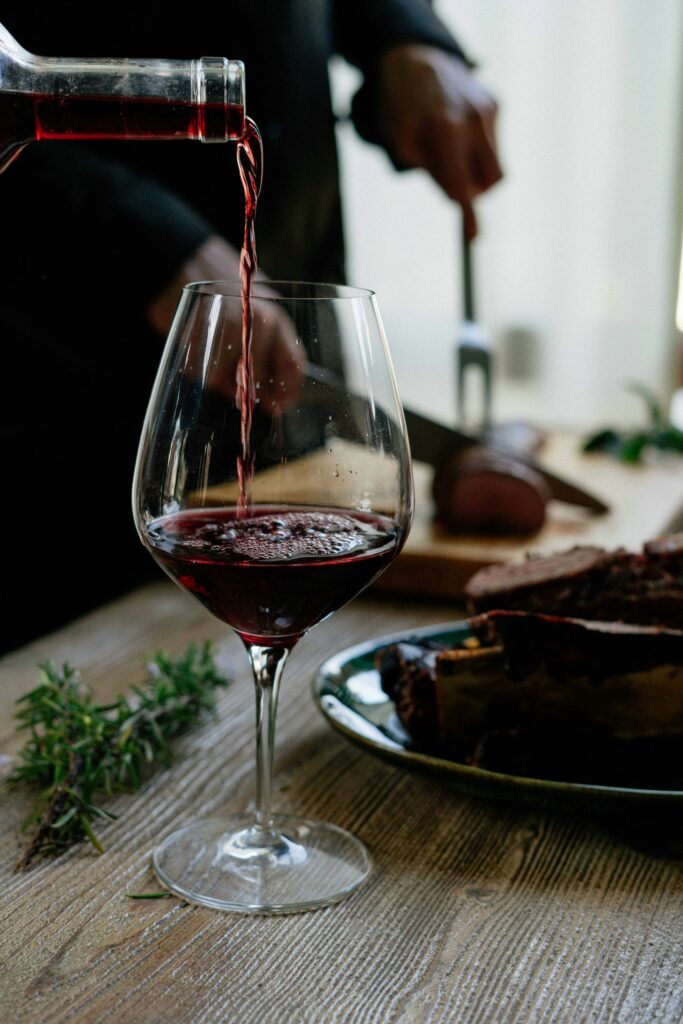Red wine pouring into glass at elegant dining table with food - serving Pinot Noir or Beaujolais for Thanksgiving wine pairing